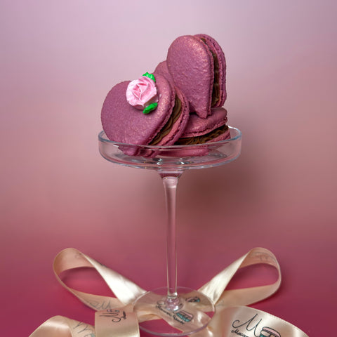 Purple macarons on a small glass stand with a pink ribbon on a pink background